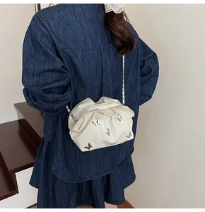 Detail of white pleated bucket bag with silver butterfly charms and delicate chain strap