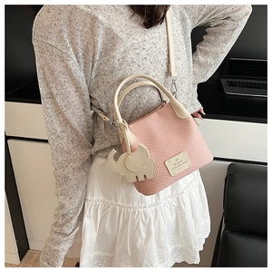 Detailed view of pink woven bucket bag with beige elephant charm and top handle