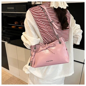 Pink glossy shoulder bag with bow detail and silver chain shown in a kitchen setting