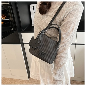 Detail of black lychee texture bucket bag with decorative elephant pendant on model