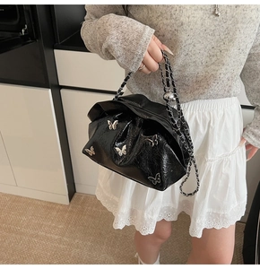 Detail of black pleated bucket bag with silver butterfly charms and metal chain strap