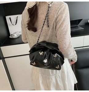 Detail of black glossy bucket bag featuring silver butterfly charms and chain strap