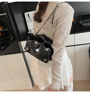 Detailed macro view of black glossy pleated bucket bag with silver butterfly metal charms