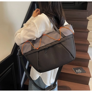 Close-up of black crossbody bag with grey plaid detail and orange elastic cord storage