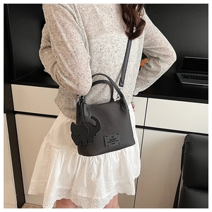 Detail of black woven bucket bag with elegant elephant charm and short handle