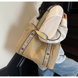 Detail of khaki canvas tote bag with wide floral woven strap and orange side label