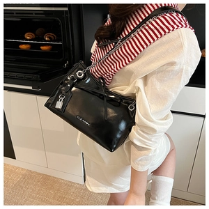 Detail of black leather shoulder bag featuring chain strap, ribbon bow, and metal lock charm