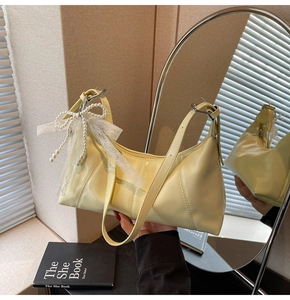 Detail of a pale yellow glossy shoulder bag with pearl and lace bow charm decoration