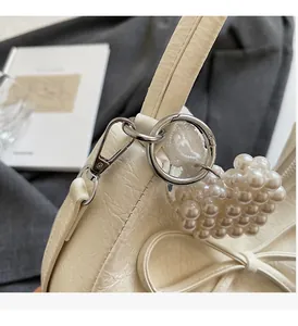 Détail d'un sac plissé crème avec pendentif cœur en perles et finitions argentées