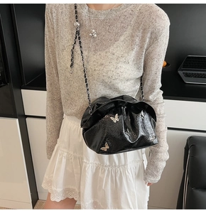Detail view of a black pleated bucket bag with silver butterfly charms and chain strap