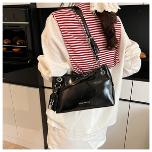 Glossy black underarm bag with silver chain and bow detail shown on a model