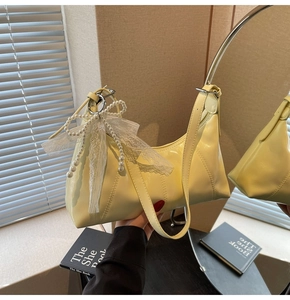 Detail of yellow patent leather hobo bag with pearl bow and white lace ribbon decoration