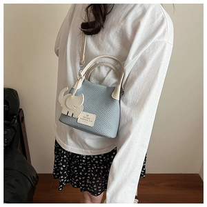 Detail of light blue textured bucket bag with cream leather straps and elephant charm