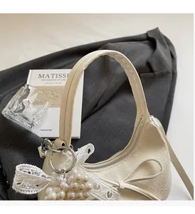 Détail du sac croissant crème avec nœud en dentelle, breloque perle et texture ridée