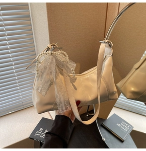 Detail of creamy white patent leather croissant bag with pearl lace bow charm
