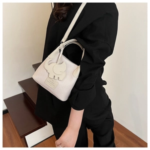 Detail of cream crossbody bucket bag with textured fabric and elephant patch on a model