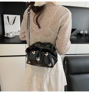 Detail of a black glossy bucket bag with silver butterfly accents worn by a model