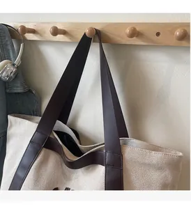 Detail of reinforced leather handles on a beige canvas tote bag in a casual setting