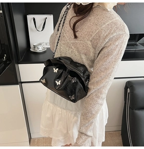 Detail of black glossy cloud bag with silver butterfly charms and chain strap on shoulder