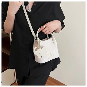 Detailed shot of white woven bucket bag with elephant charm and metal logo plate