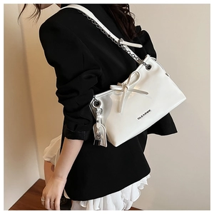 White shoulder bag with bow detail, chain strap, and logo on model in black suit