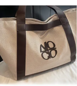 Close-up of beige canvas tote bag with brown leather handles and NOCO logo detail