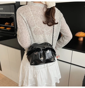 Detail of black pleated bucket bag with silver butterfly charms worn by a model