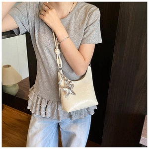 Détail du sac seau en cuir verni crème avec pendentif étoile et bandoulière nouée