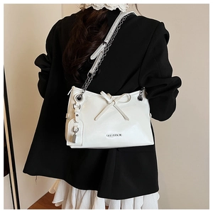 Detailed view of white patent leather shoulder bag with silver chain and bow detail