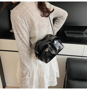 Detail of black pleated leather bucket bag with silver butterfly charms and chain strap