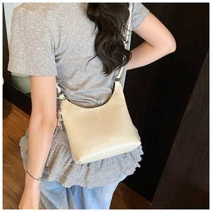 Détail du sac bandoulière en cuir verni crème avec anneau métallique et logo