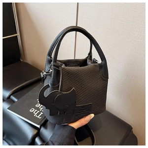Detail of black woven bucket bag featuring an elephant leather charm and sleek metal hardware