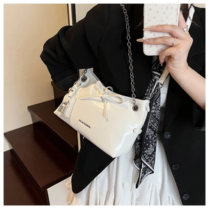 Detail of white patent leather shoulder bag with silver chain and bow charm on model