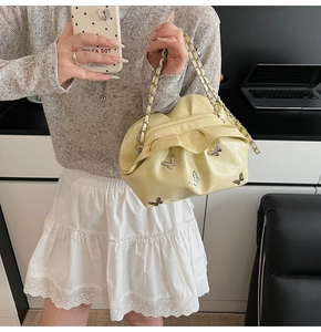 Detail of light yellow pleated cloud bag with metallic butterflies and silver chain strap