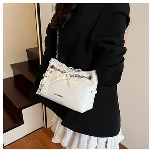 Detail of white patent leather shoulder bag with metal chain bow and lock pendant