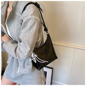 Détail du sac seau noir avec texture brillante, breloque étoile et bandoulière nouée