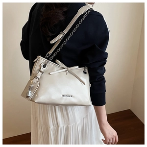 Détail d'un sac à bandoulière beige avec nœud papillon, chaîne élégante et breloque cadenas dorée