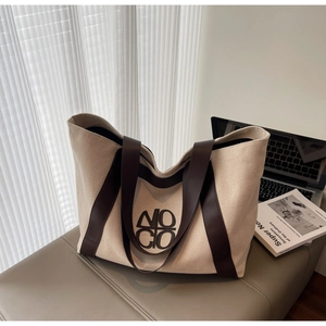 Detailed view of canvas tote bag with leather handles and NOCIO logo on a soft bench