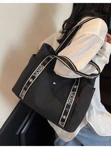 Large black canvas tote bag with floral letter straps shown on a model for daily use