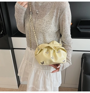 Detail view of cream bucket bag with pleated texture and silver butterfly charms