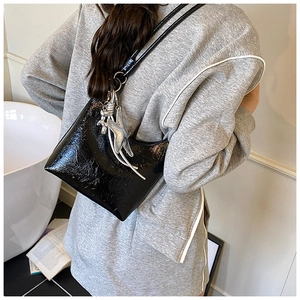 Détail d'un sac seau en cuir verni plissé noir avec breloques argentées sur un mannequin