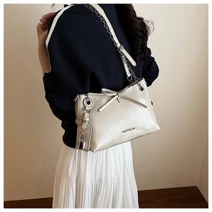 Close-up of a cream shoulder bag with a bow detail and a stylish metal chain strap