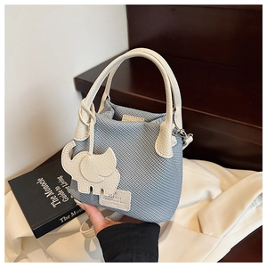 Detail of light blue textured bucket bag with white leather handle and elephant charm