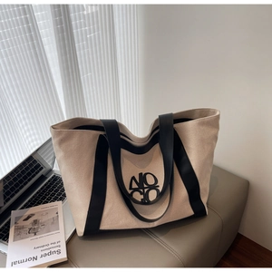 Detail of a large beige canvas tote bag with black leather straps on a grey soft stool