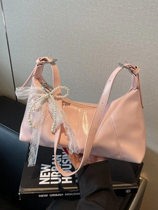 Pink glossy leather shoulder bag with lace bow and pearl chain on a book background