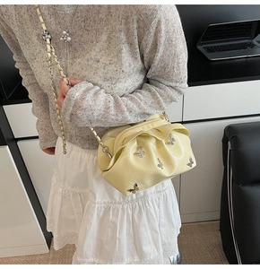 Detail of beige pleated cloud bucket bag with silver butterfly charms and chain strap