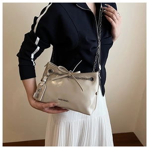 Detail of a creamy white underarm bag featuring a metallic chain and bow decoration