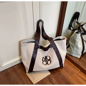Close-up of canvas tote bag with brown leather handles and logo by a vintage mirror