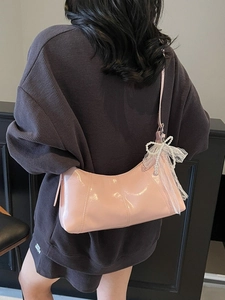 Pink glossy hobo shoulder bag with pearl bow pendant and pleat details on model