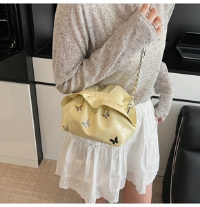 Detail of light yellow pleated bucket bag with butterfly charms and silver chain strap